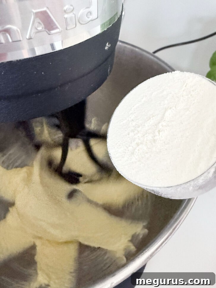 All-purpose flour being gently sprinkled into the creamy batter inside the mixing bowl, awaiting thorough mixing.