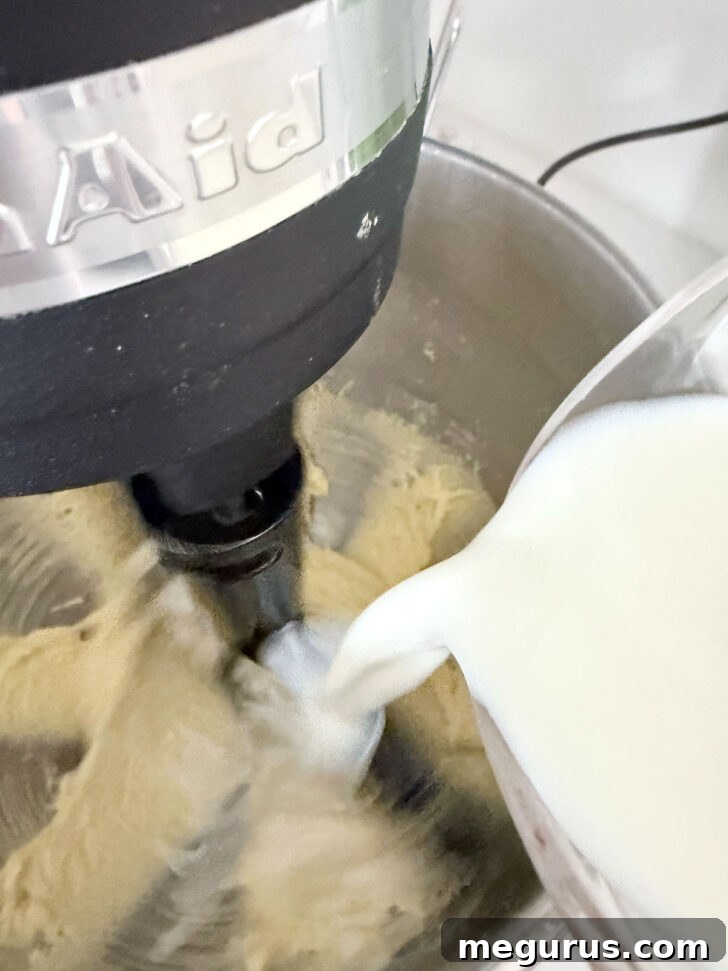 Pouring fresh milk into the lemon batter in the mixing bowl, preparing for the final liquid additions.