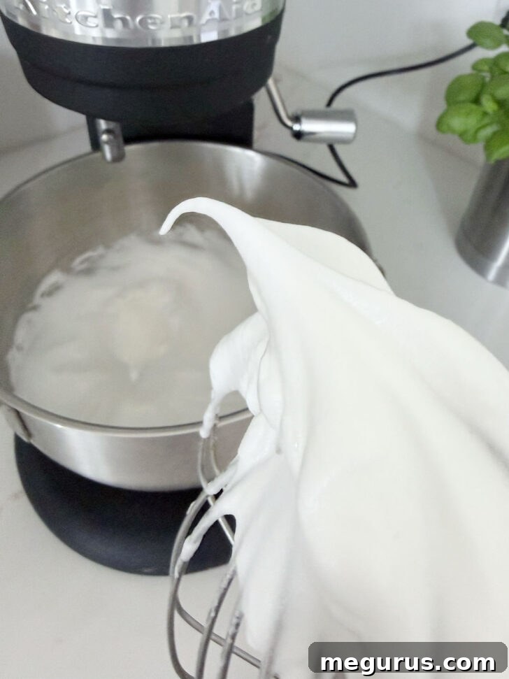 Perfectly whipped egg whites forming stiff, glossy peaks in a mixing bowl, ready to be folded into the batter.