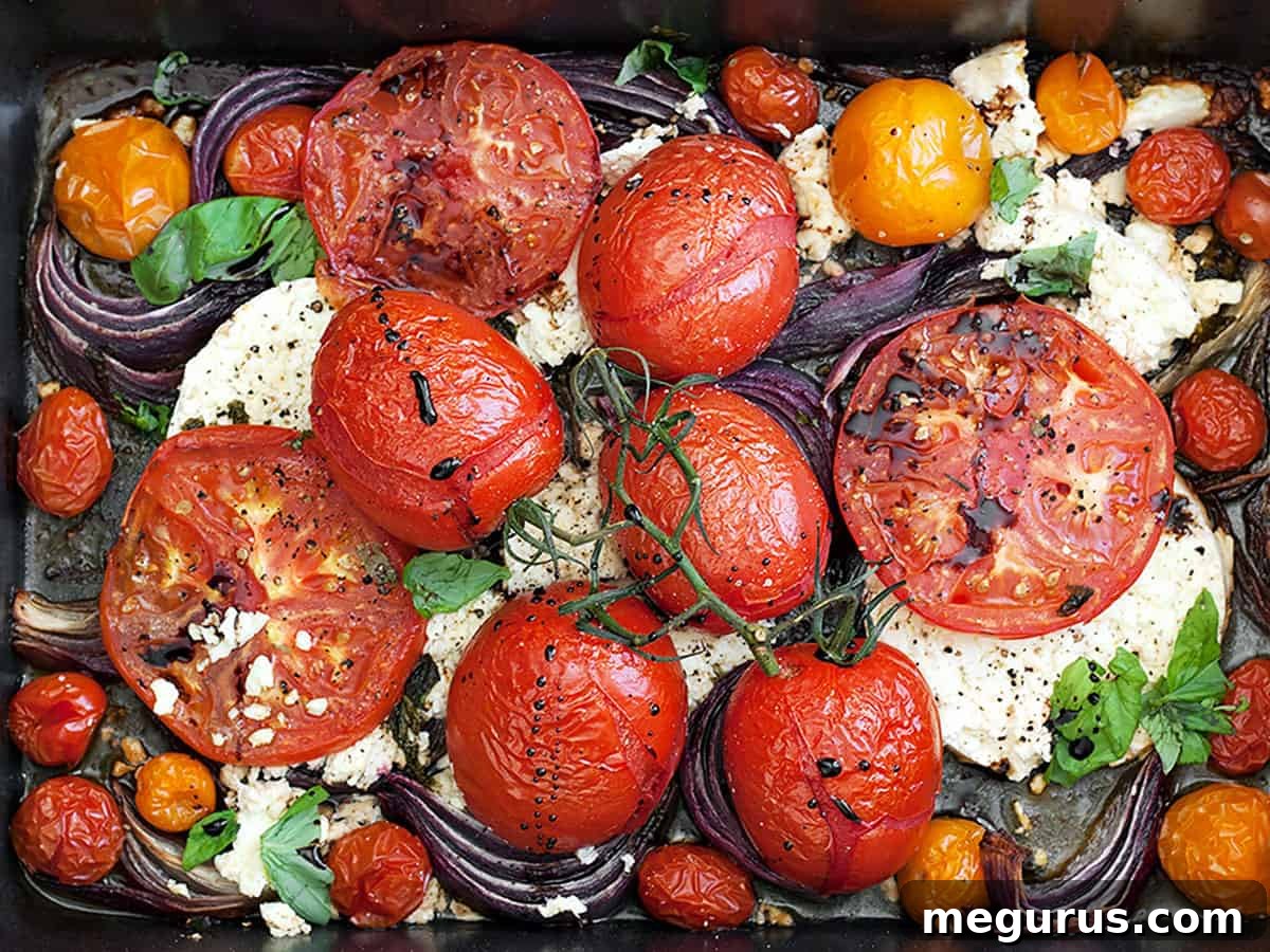 A close-up of roasted tomatoes and crumbled feta cheese in a roasting pan, garnished with fresh herbs.
