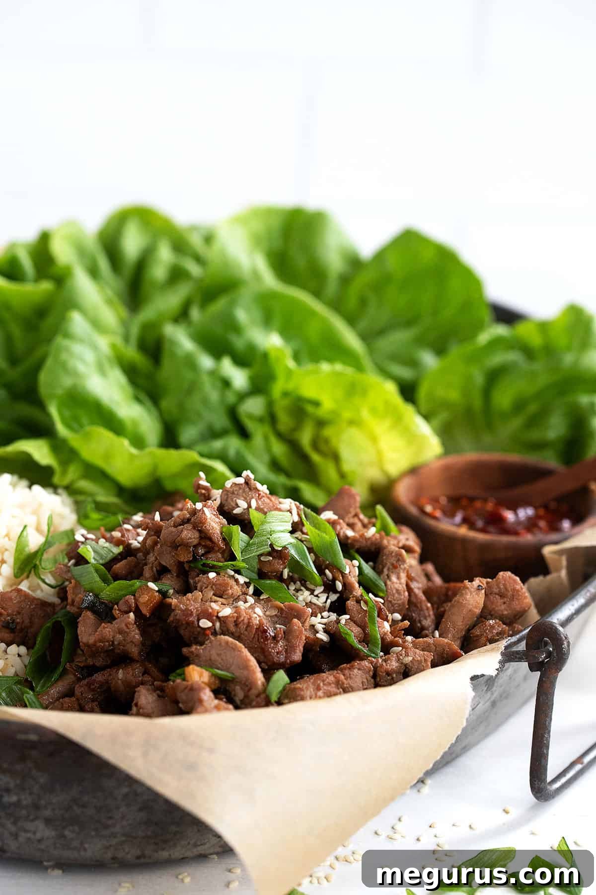 A large platter of Korean pork bulgogi served with bowls of white rice and fresh lettuce leaves, inviting guests to make their own wraps.