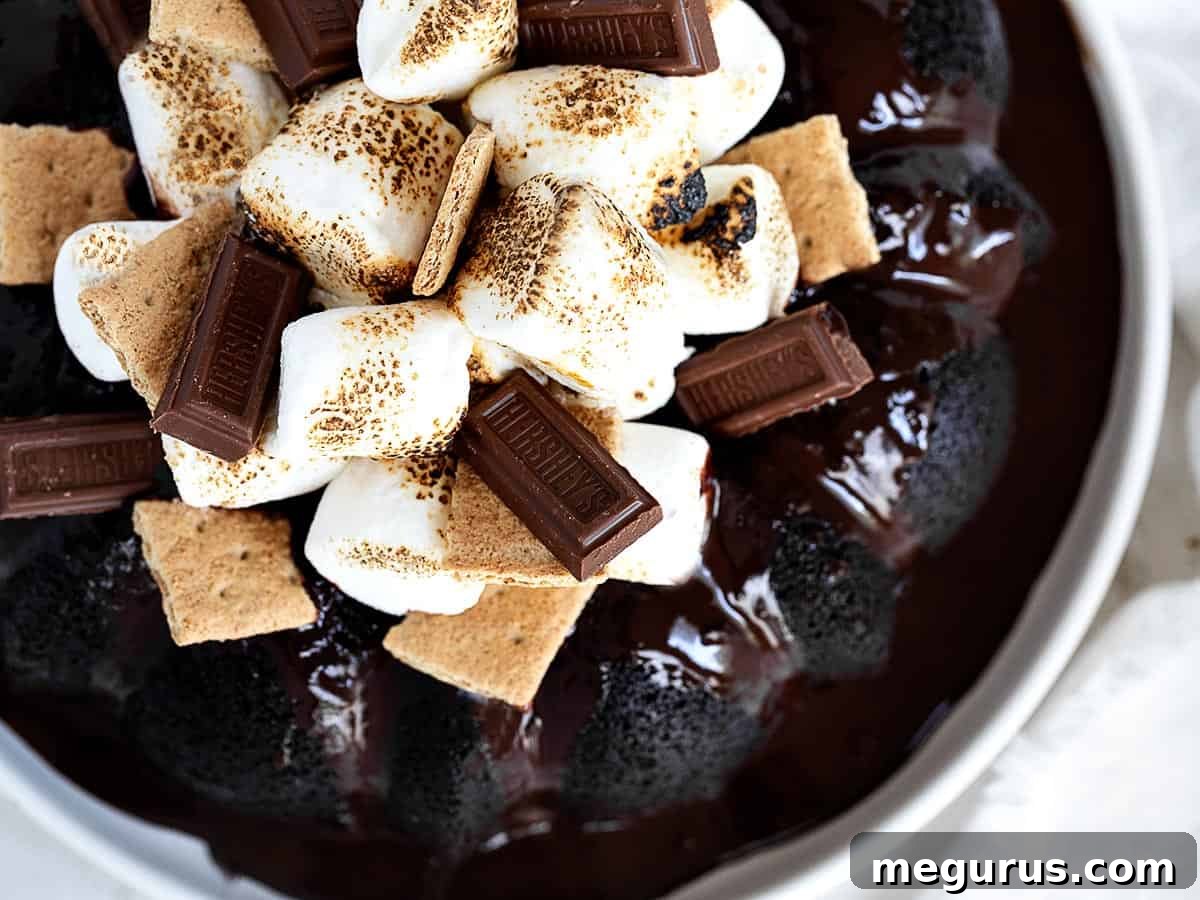 s'mores bundt cake on plate with marshmallows, graham crackers and hershey bar pieces on top