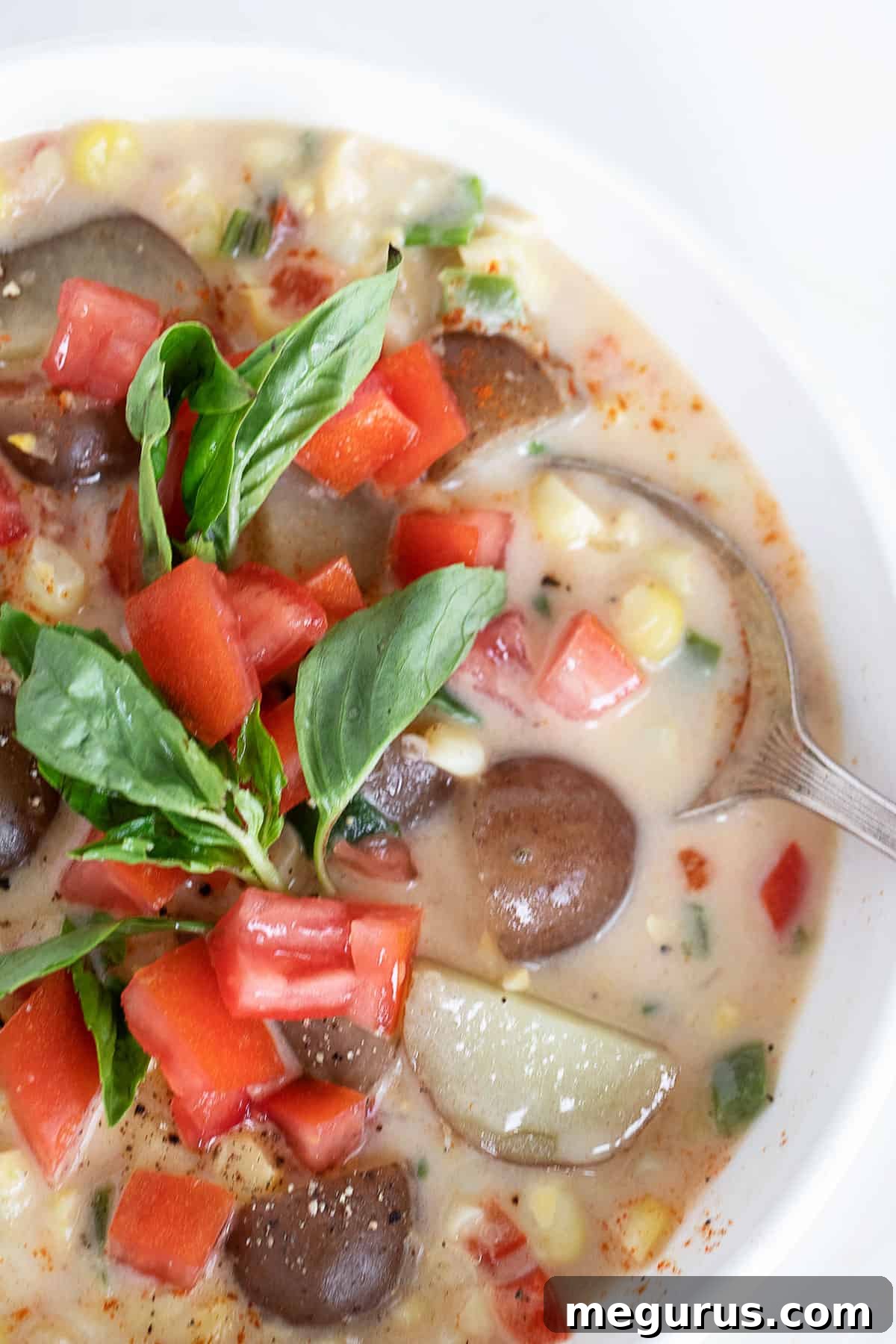 A close-up shot of a white bowl filled with creamy Summer corn chowder, garnished with fresh basil.