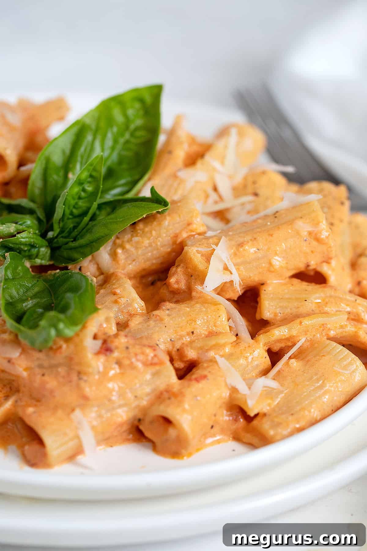 Close-up of Creamy Roasted Red Pepper Pasta garnished with fresh basil on a white plate