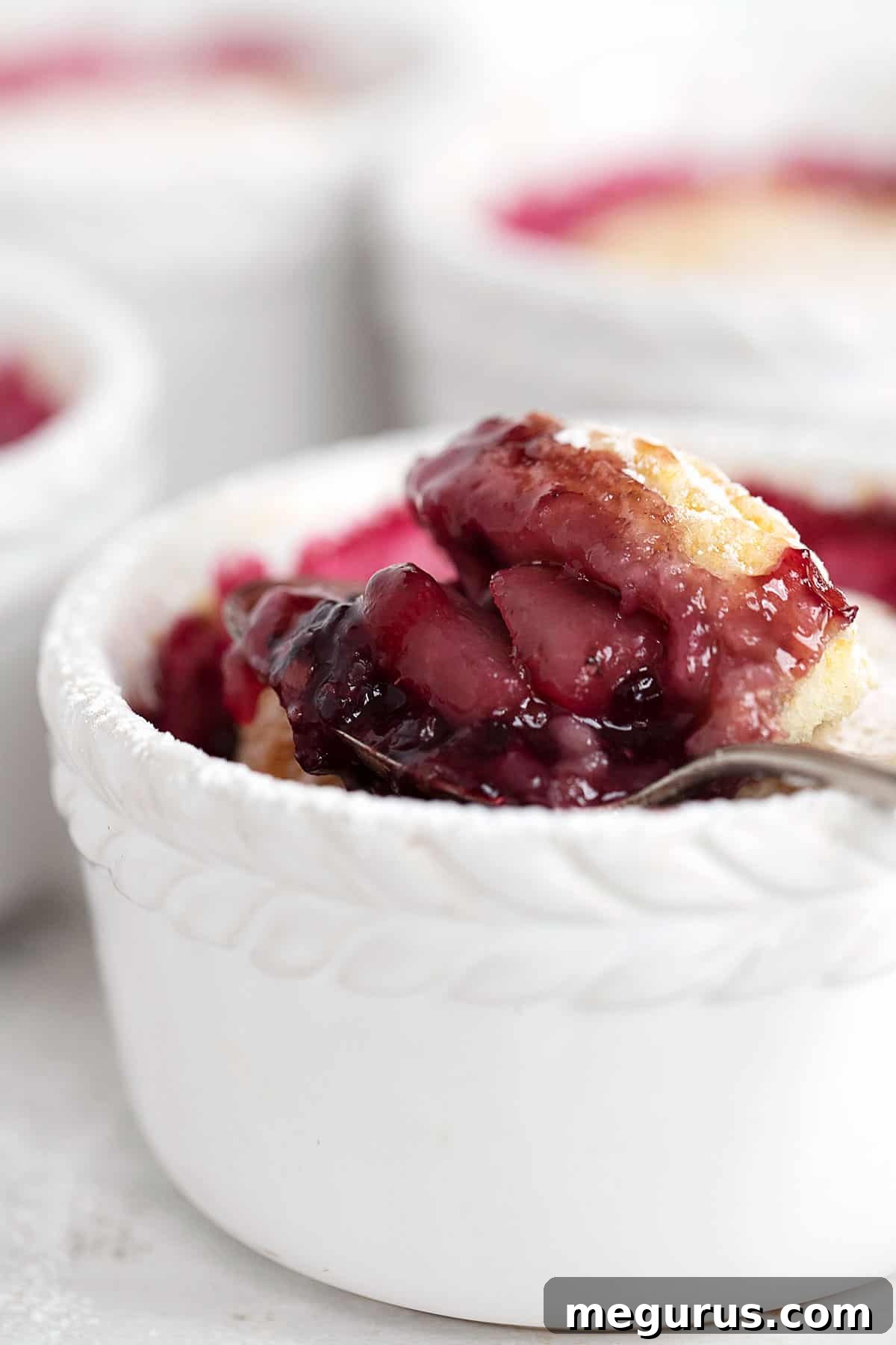 A close-up of a rustic blackberry pear cobbler in a ramekin, highlighting the golden-brown topping and fruit.