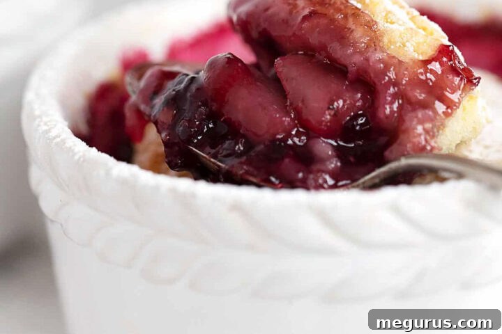 Blackberry pear cobbler in a ramekin with a spoon, ready to be enjoyed.