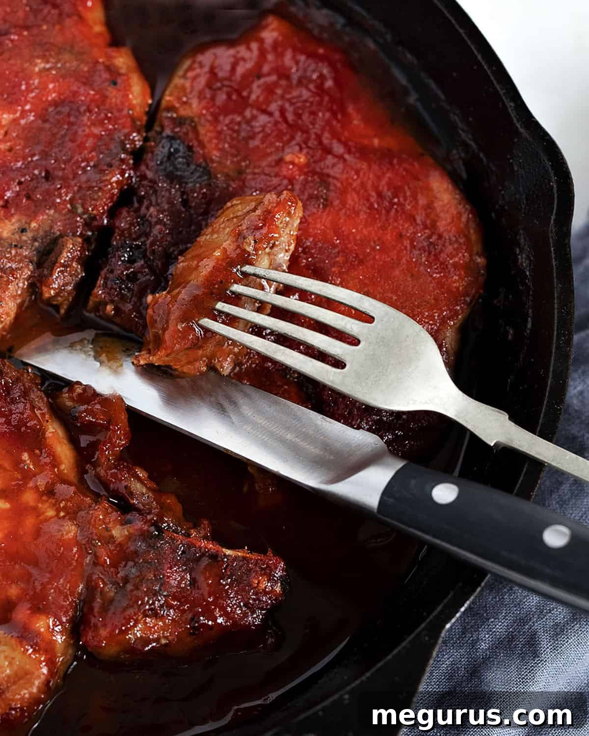 close-up of baked bbq pork chops in cast iron skillet, garnished with fresh herbs