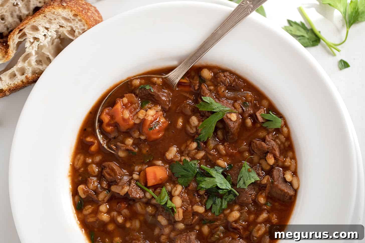 Classic Beef and Barley Soup in a white bowl, served with crusty bread on the side