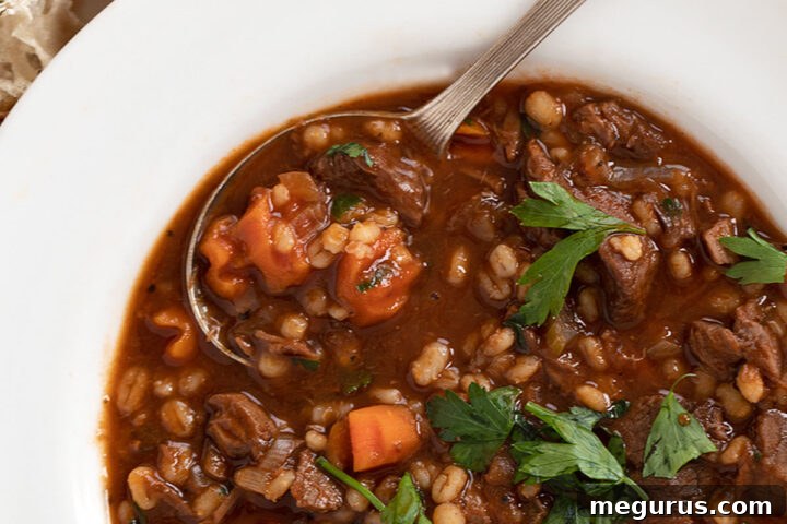 Hearty Beef and Barley Soup in a white bowl with bread on the side, ready to be enjoyed.