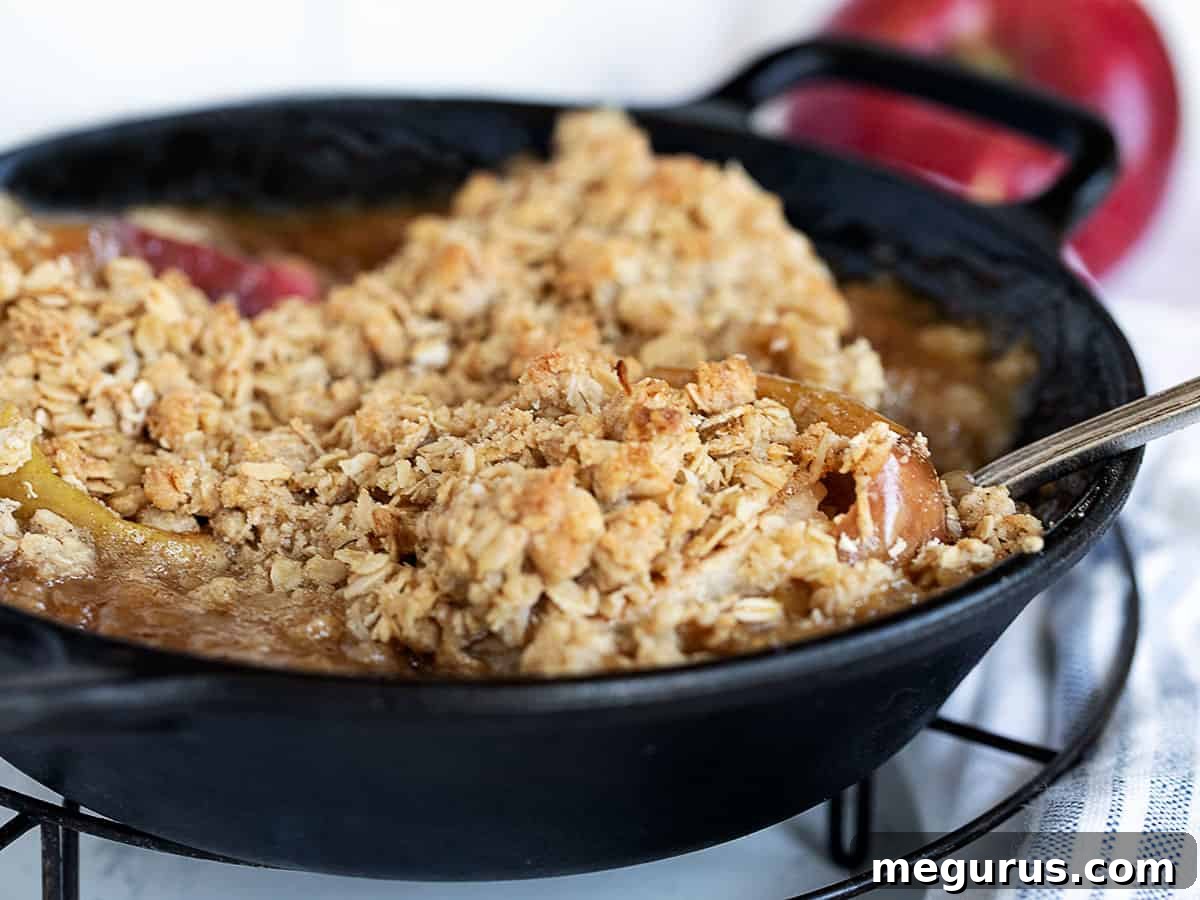 Delicious baked apples topped with golden oat crumble, served hot in a rustic cast iron skillet – a perfect fall dessert.