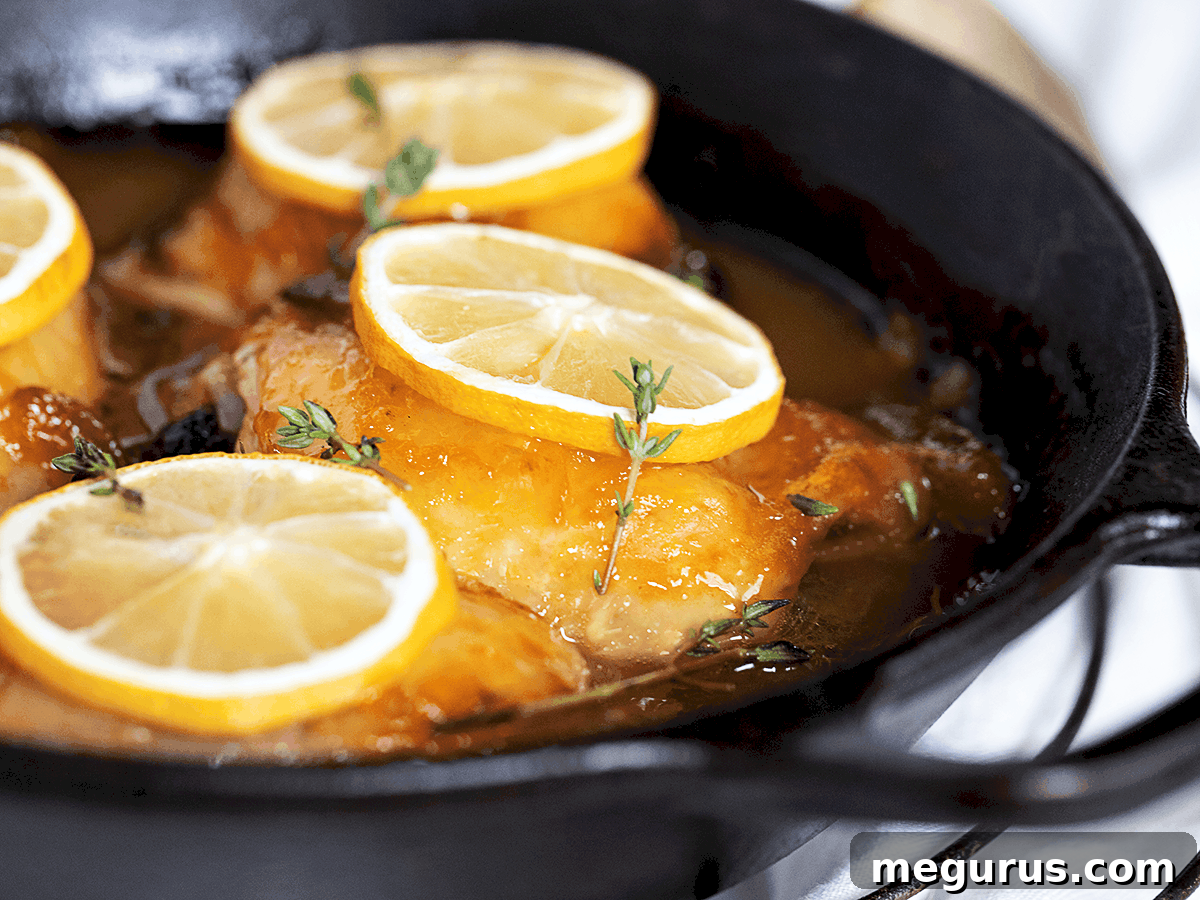 Golden glazed lemon chicken thighs in a pan with fresh lemon slices, ready to serve.