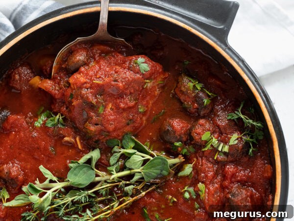 Rich Chicken Cacciatore simmering in a pan, ready to serve, adorned with fresh herbs