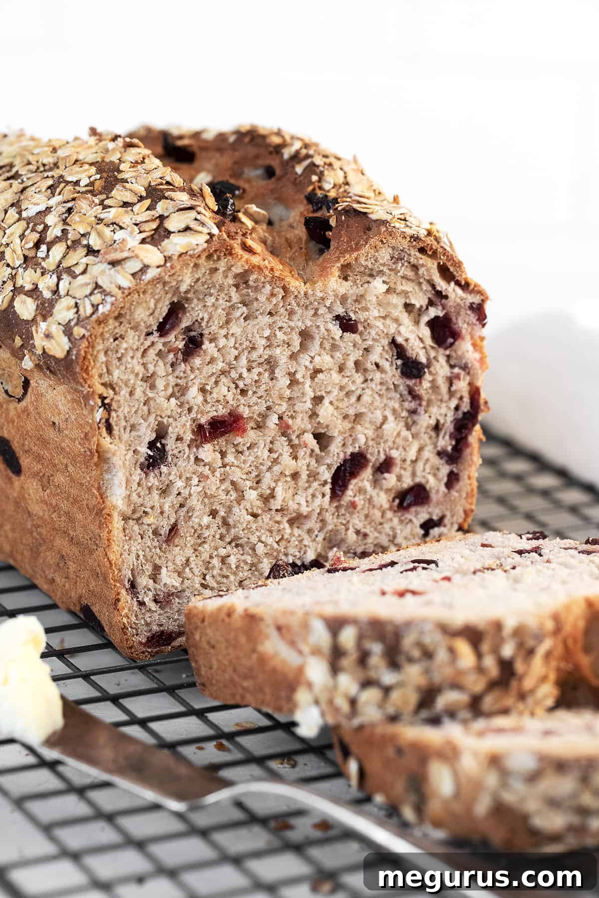 Close-up of a sliced cranberry oatmeal bread on a cooling rack, showing the texture and distribution of cranberries.
