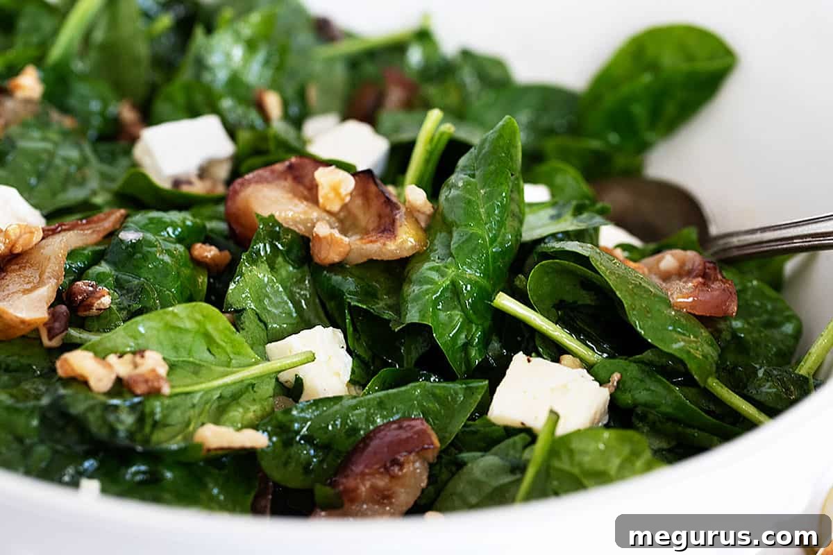 warm spinach salad in bowl with roasted apples and brie