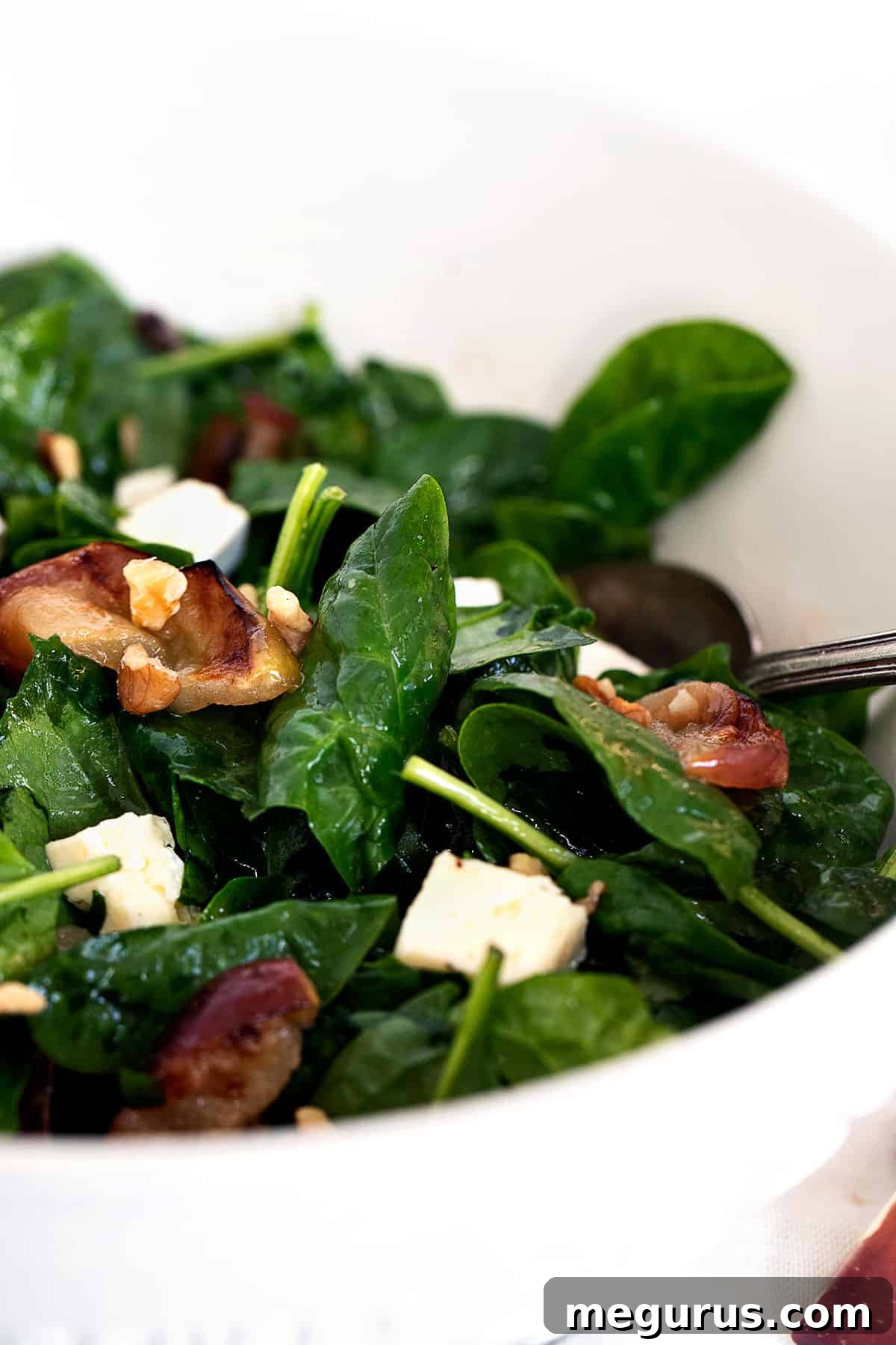 warm spinach salad in bowl with roasted apples and brie