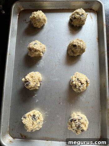 Perfectly portioned oatmeal raisin cookie dough balls arranged on a parchment-lined baking sheet, spaced adequately for even baking.