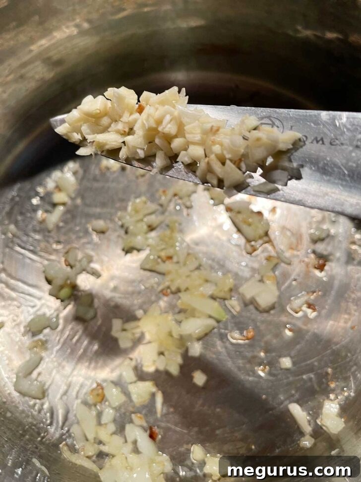 Adding minced garlic to a pot of sautéed onions.