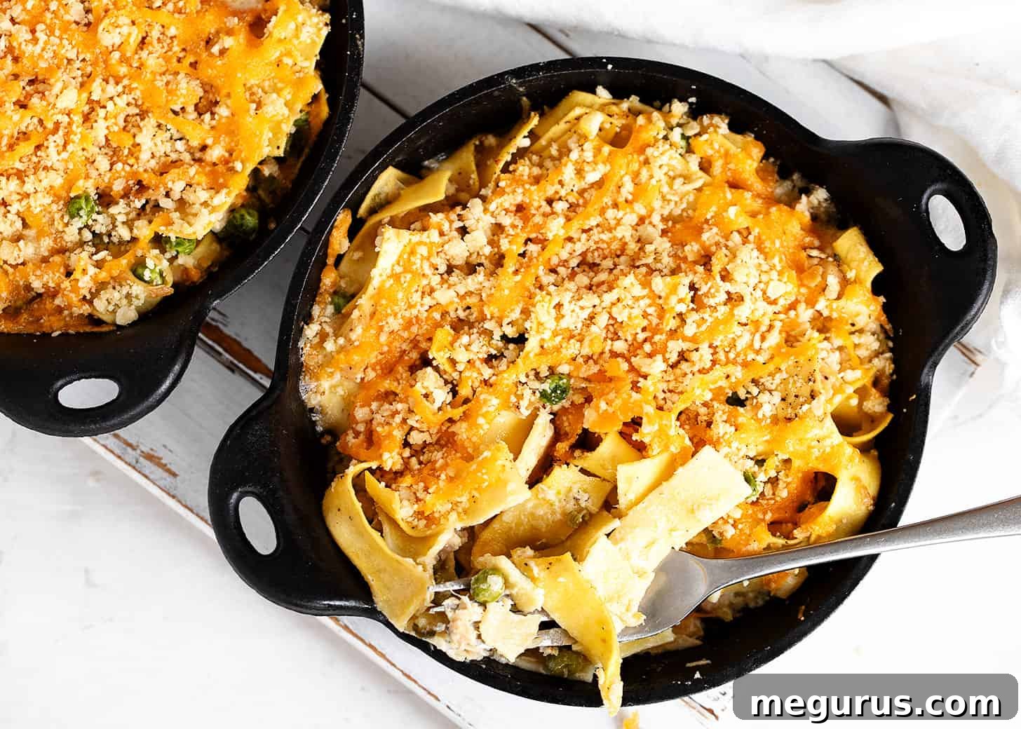 Two mini cast iron skillets filled with golden-brown tuna casserole, ready to be served