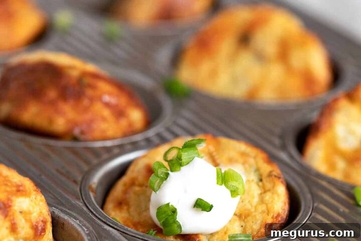 Golden-brown Muffin Tin Mashed Potatoes in a muffin tin, served with sour cream and green onion on top.