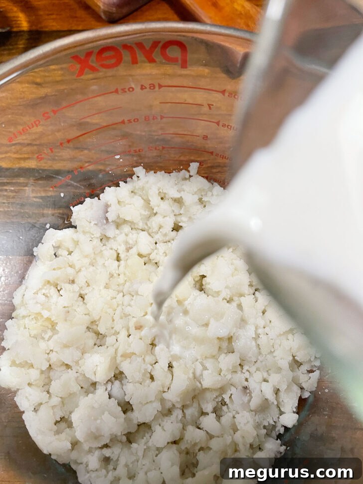 Pouring milk into a bowl of cooled mashed potatoes.