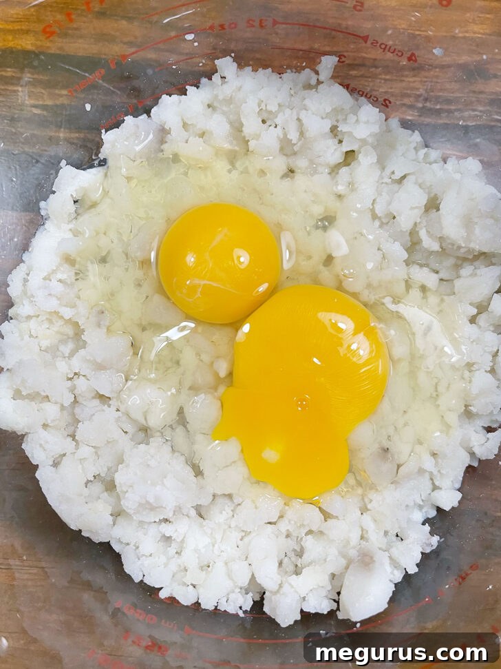 Adding two large eggs to the mashed potato mixture in a bowl.