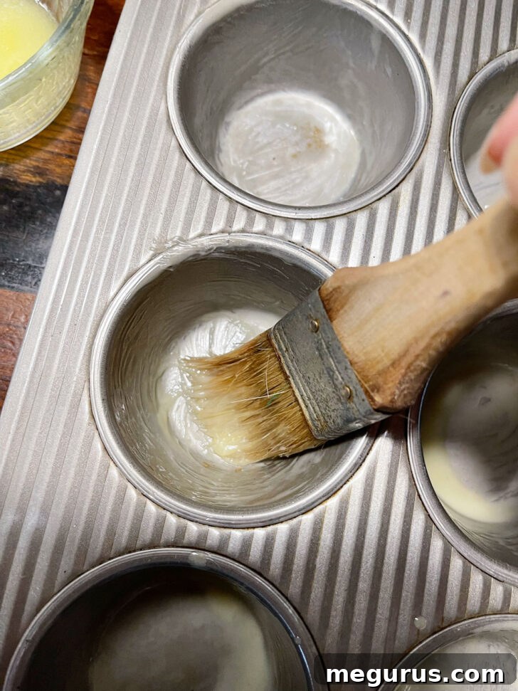 Brushing muffin tin cups with melted butter to prevent sticking.