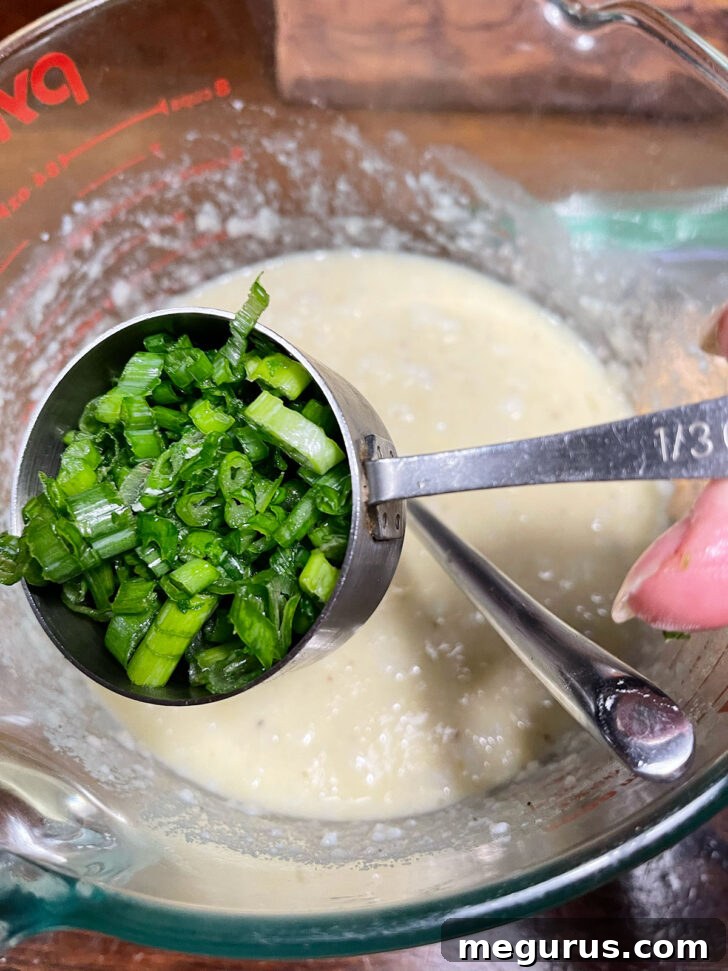 Adding chopped green onions to the potato batter.