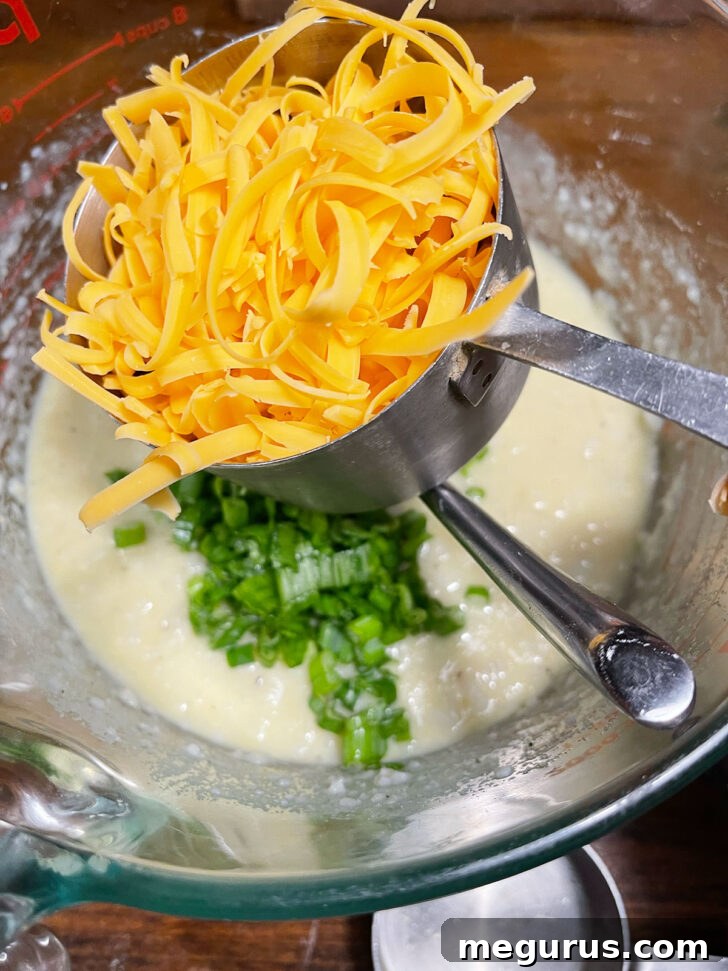 Mixing shredded cheddar cheese into the mashed potato batter.