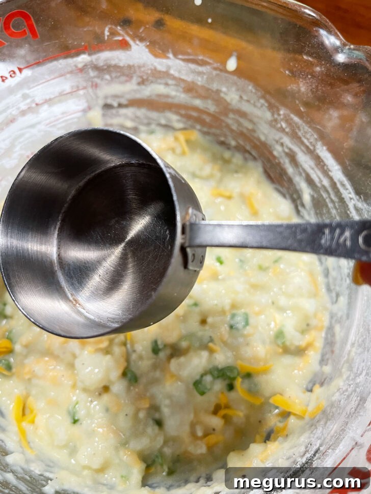 Scooping the mashed potato batter into a muffin cup using a 1/4 cup measure.