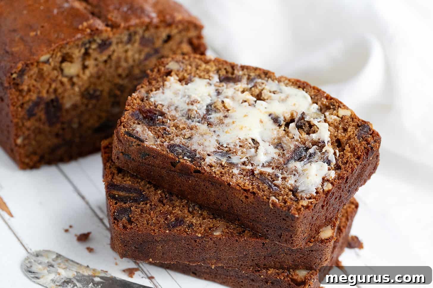 Perfectly sliced date nut bread with a pat of butter, showing a moist, rich crumb and visible nuts.