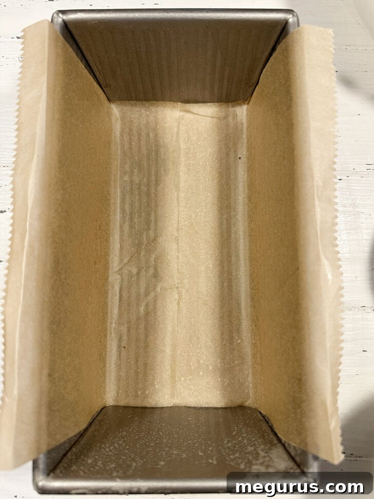 A metal loaf pan being lined with parchment paper.