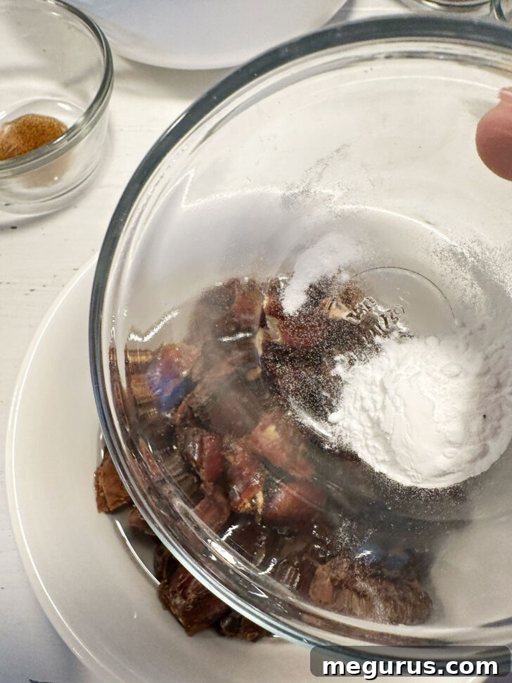 Baking soda being added to a bowl of chopped dates and boiling water.