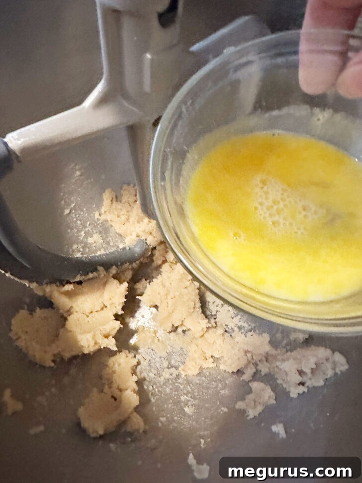 A lightly beaten egg being added to the creamed butter and sugar mixture.