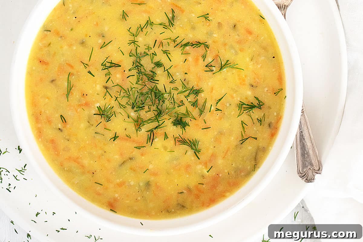 Traditional Polish potato and dill pickle soup (Zupa Ogórkowa) served in a white bowl with a spoon, garnished with fresh dill.