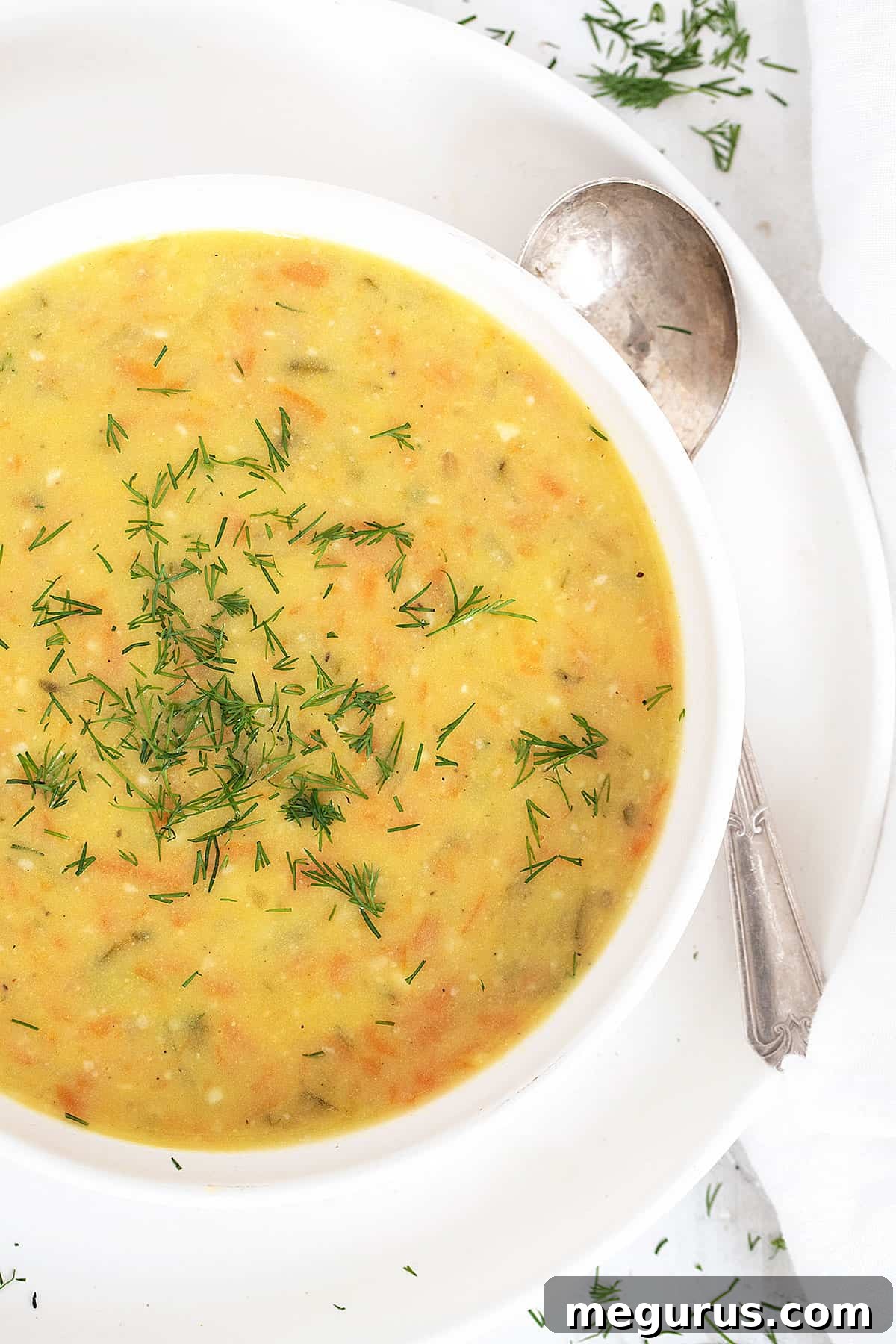 Close-up of Polish potato and dill pickle soup in a white bowl, garnished with fresh dill and a spoonful of sour cream.