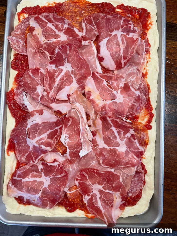 Italian deli meat, likely Prosciutto Cotto, scattered onto the tomato-covered pizza dough.