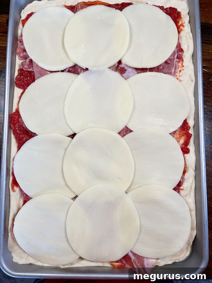 Slices of Provolone cheese placed meticulously onto the meat layer of the parigina.