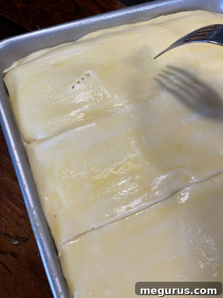 A fork pricking the puff pastry multiple times to create small holes before baking.