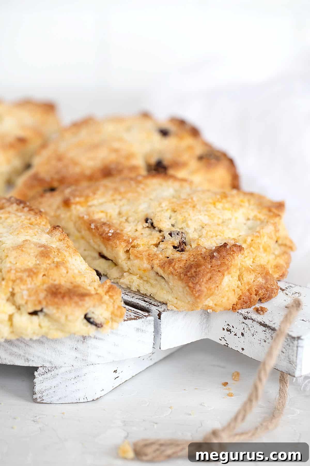 Close-up of golden-brown cranberry orange scones, garnished with coarse sugar, on a wooden tray.