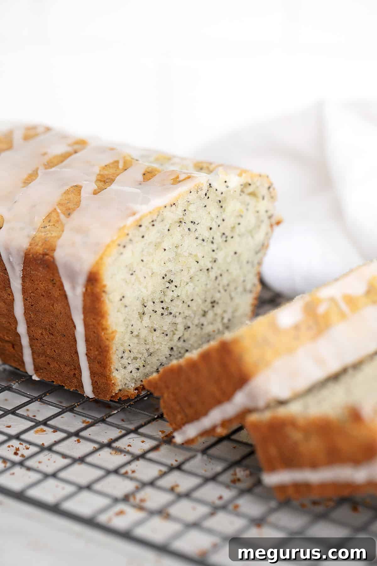 Close-up of a beautifully sliced lemon poppy seed loaf with a glistening lemon glaze on a cooling rack