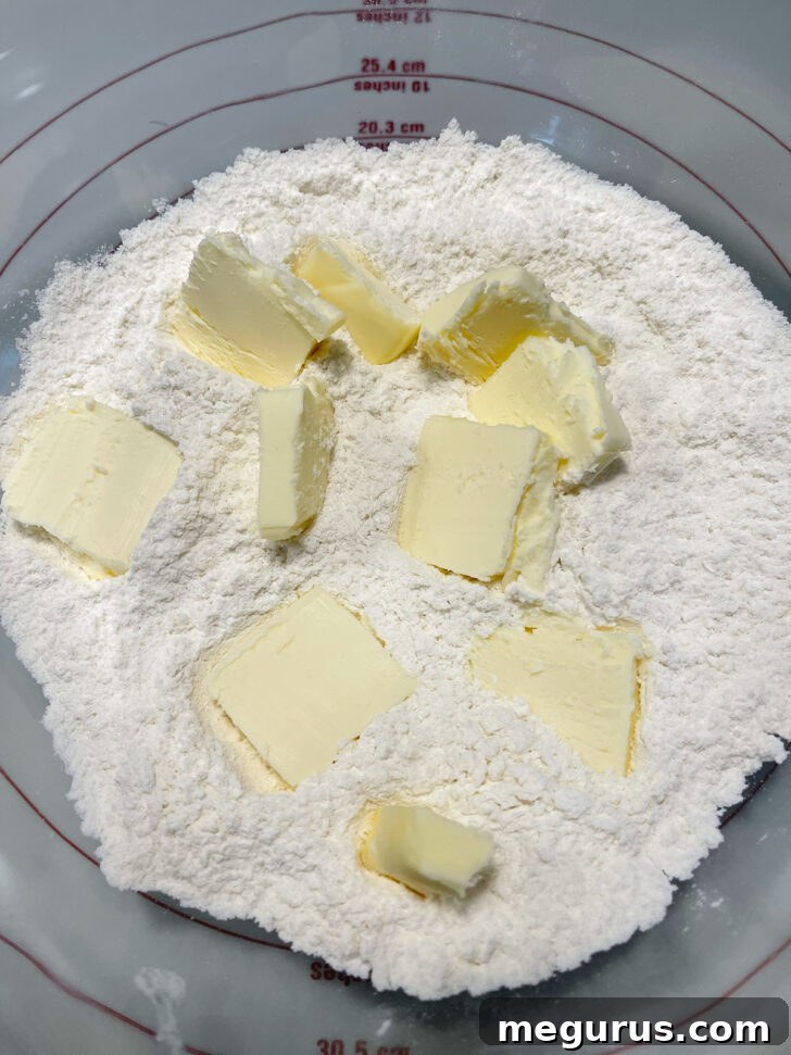 Adding cold, cubed butter to the dry flour mixture in a large mixing bowl.