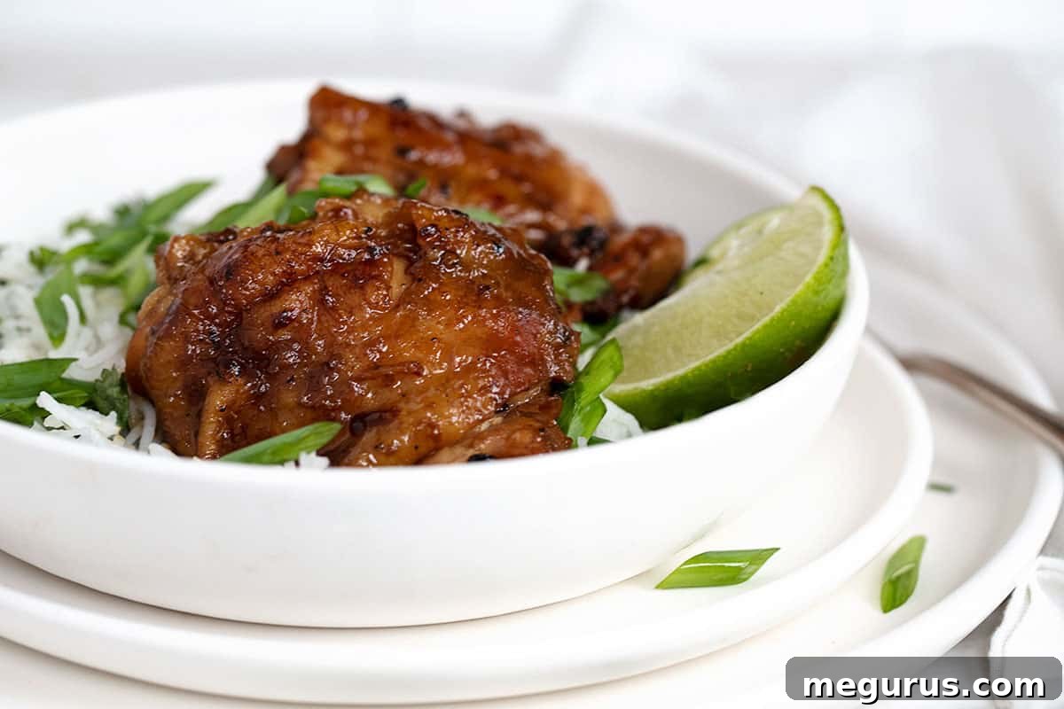 Filipino Chicken Adobo with coconut milk served in a bowl with rice and garnished with green onions and lime wedges.