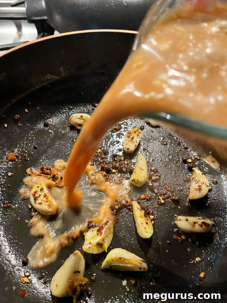 Adding adobo sauce to a skillet with garlic and peppers.