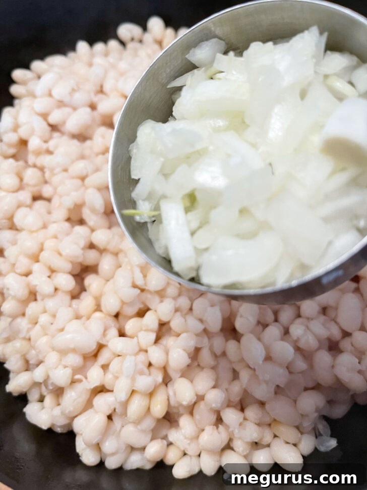 Drained beans in baking dish, with onions being added