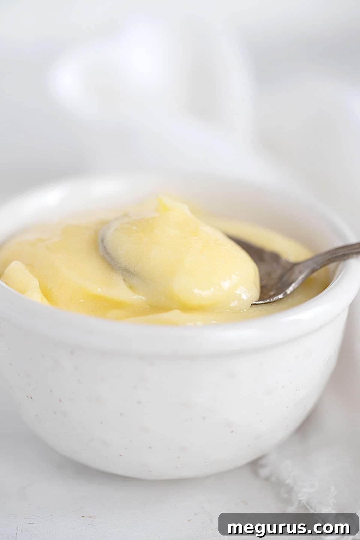 Small white bowl filled with creamy lemon curd, with a spoon resting in it.