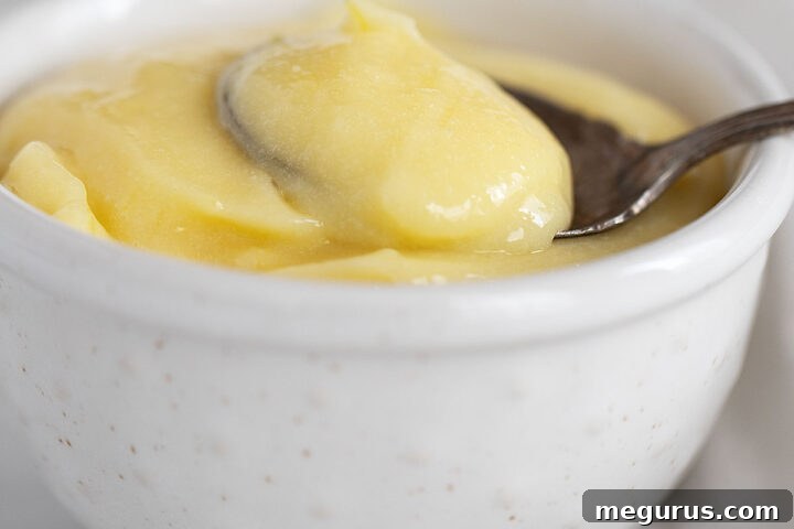 Whole egg lemon curd in a small white bowl with a spoon, ready to be served.