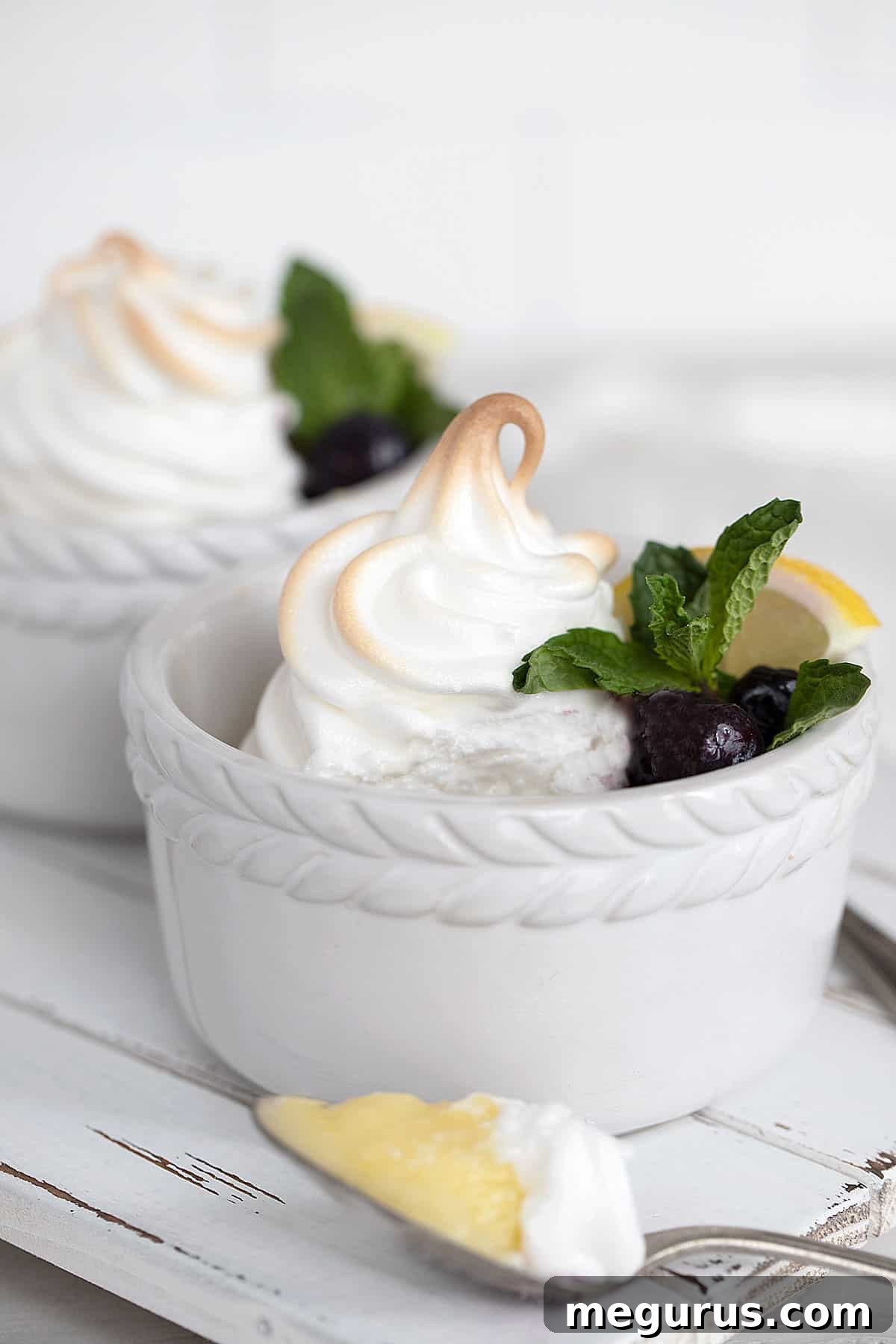 Individual lemon meringue pudding in a white ramekin, beautifully topped with meringue and fresh blueberries.