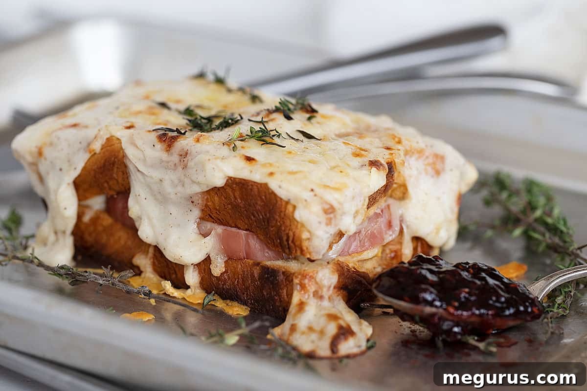 Classic Croque Monsieur sandwich on a baking sheet, with a spoonful of raspberry jam nearby