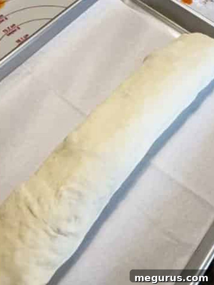A fully rolled stromboli placed on a parchment-lined baking sheet, ready for the oven.