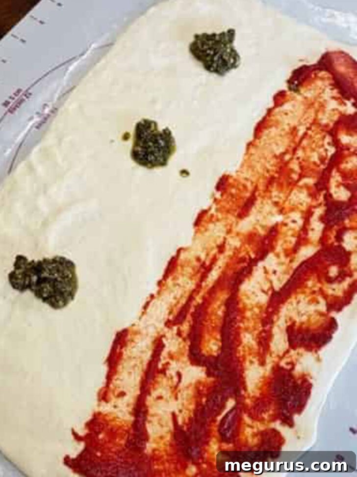 Adding dollops of vibrant basil pesto to the other half of the stromboli dough.